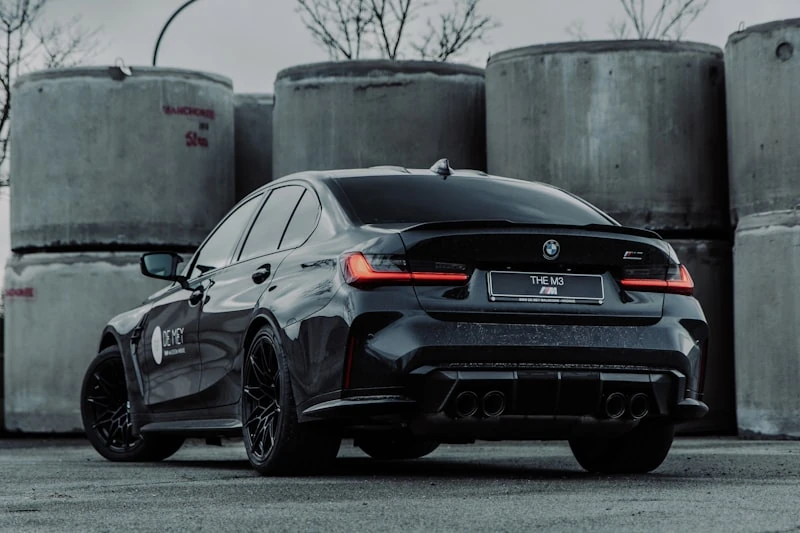 Black BMW M3 Competition from the rear three-quarter in an industrial yard